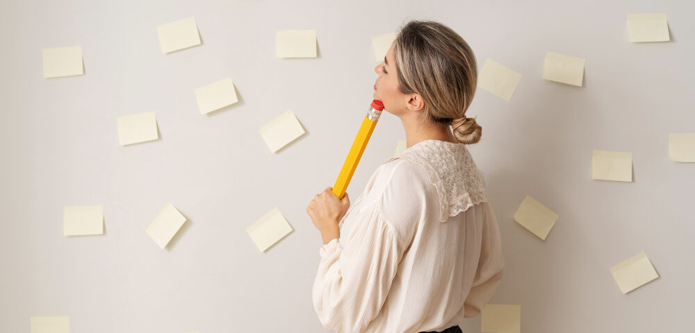 uma mulher segurando um lápis e olhando para uma parede cheia de post-its