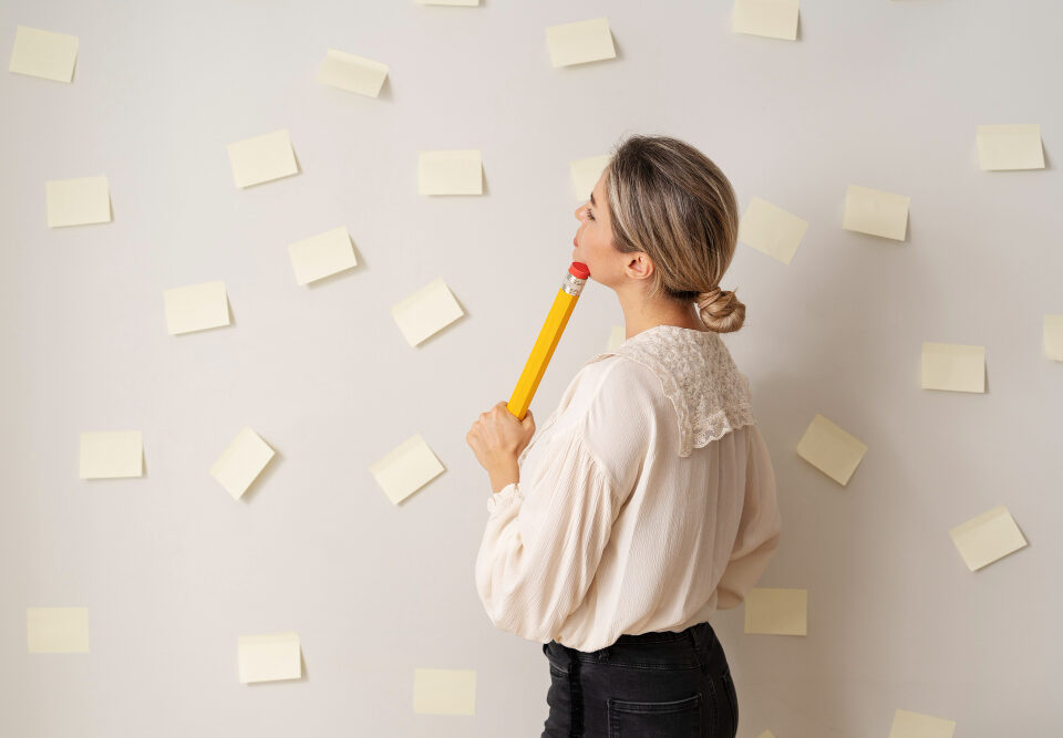 uma mulher segurando um lápis e olhando para uma parede cheia de post-its